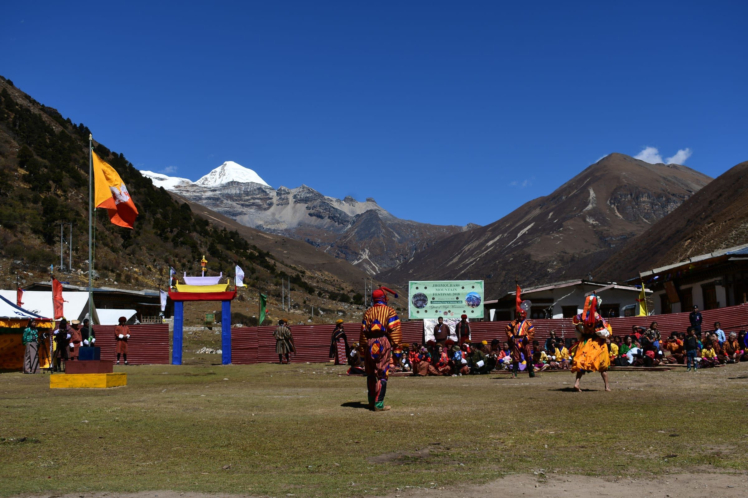 Dancers perform on an open field below a snow-capped mountain.